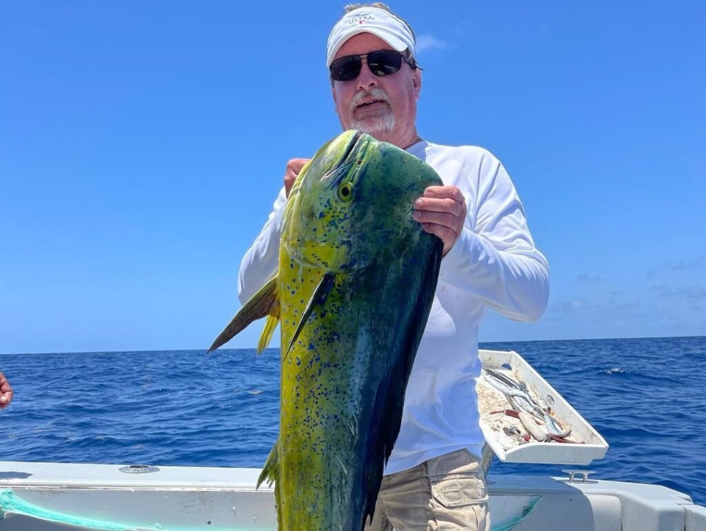 An angler proudly holds up a large, vibrant mahi-mahi on a boat, showcasing the success of "mahi mahi Key West fishing charters". The deep blue ocean and clear sky in the background highlight the excitement and rewarding experience of fishing for mahi-mahi in the beautiful waters of Key West.