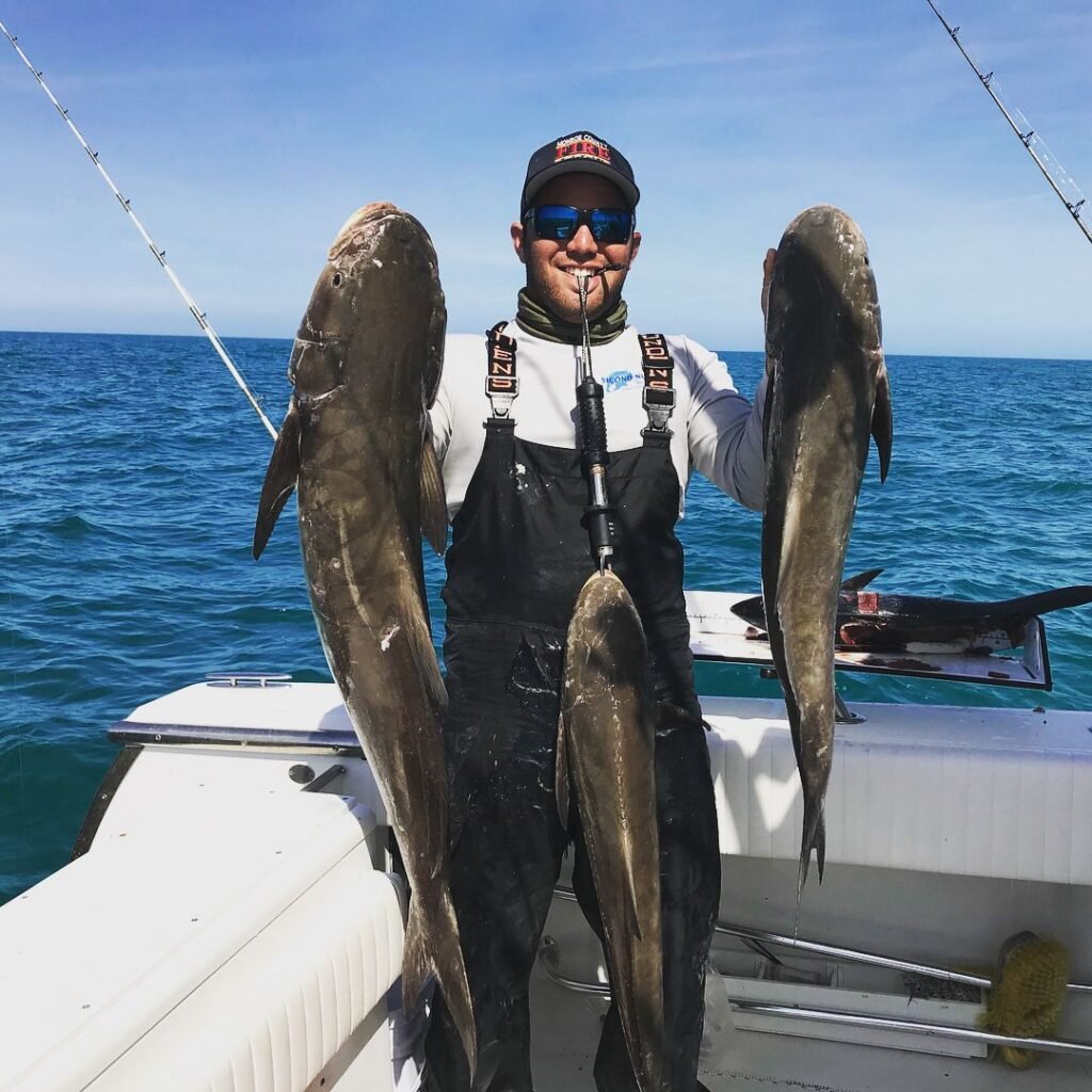 Angler holding three large cobia on a boat during a successful Cobia Fishing Charter in Key West with Fish Daily Charters, with the turquoise ocean and clear sky in the background.