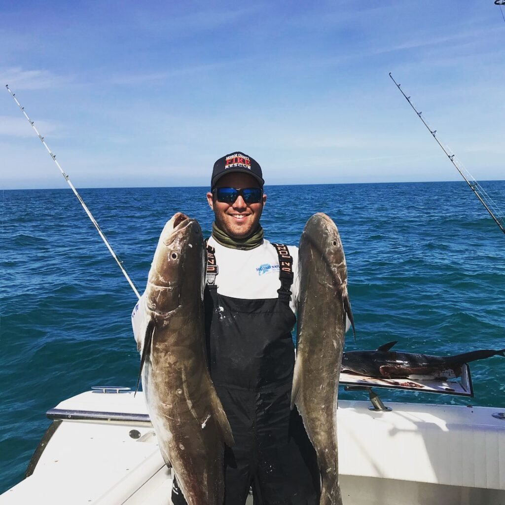 Angler proudly holding two large cobia on a boat during a successful Cobia Fishing Charter in Key West with Fish Daily Charters, with the calm ocean and clear sky in the background.
