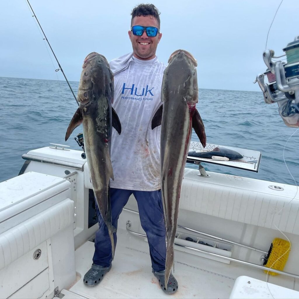 Angler proudly holding two large cobia on a boat during a successful Key West Cobia Fishing Charter with Fish Daily Charters, with the open ocean and cloudy sky in the background.