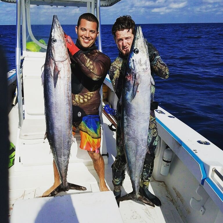 Two proud anglers holding large king mackerels on a boat during a successful Key West King Mackerel Fishing Charter with Fish Daily Charters, with the deep blue ocean in the background.