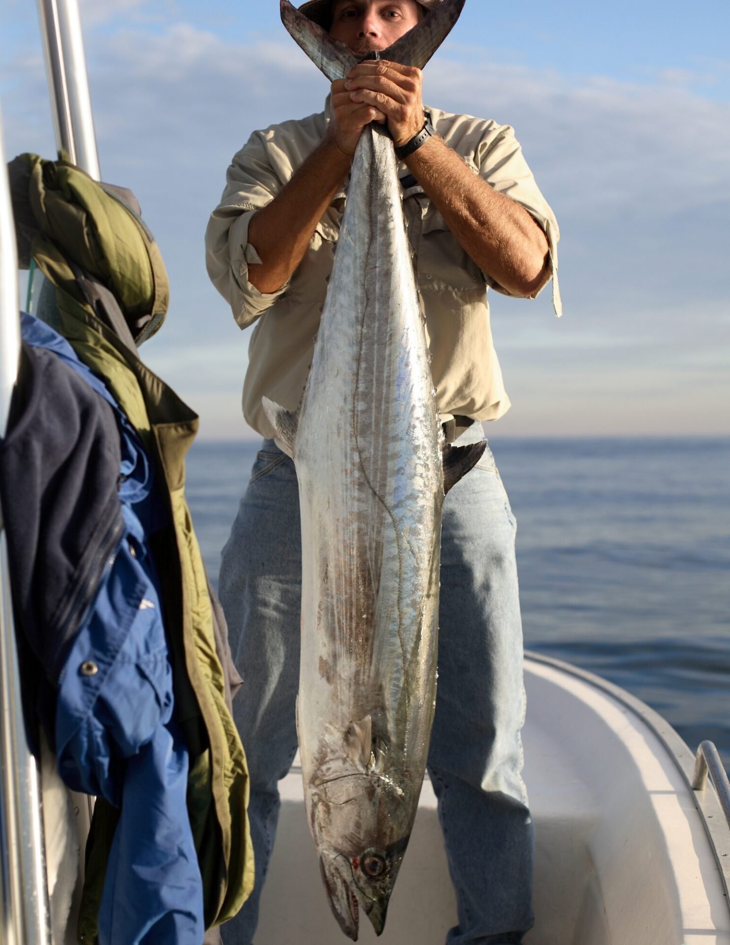 Angler holding a large king mackerel vertically on a boat during a Key West King Mackerel Fishing Charter with Fish Daily Charters, with the calm ocean and a soft evening sky in the background.