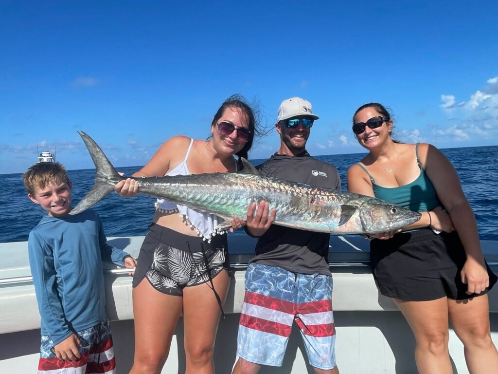 Family proudly holding a large king mackerel on a boat during a King Mackerel Fishing Charter in Key West with Fish Daily Charters, with the open ocean and clear blue sky in the background.