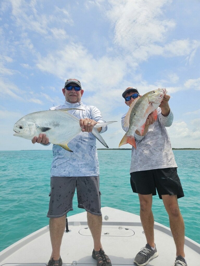 Two proud anglers display their impressive catches—a permit fish and a snapper—against the picturesque backdrop of Key West's turquoise waters and blue sky, highlighting the excitement of 'Permit Fishing Charters in Key West'. This image captures the joy and success of a productive fishing trip, showcasing the diverse and rewarding fishing opportunities available in the area.