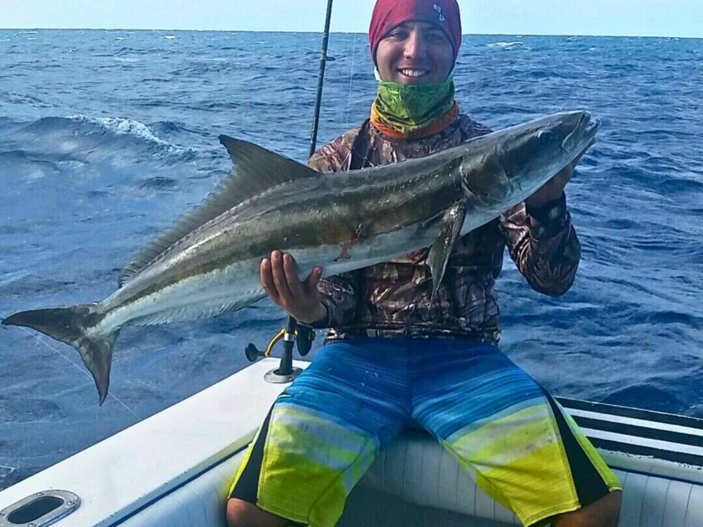 Key West Cobia Fishing Charters 1 Angler smiling while holding a large cobia on a boat during a Key West Cobia Fishing Charter with Fish Daily Charters, with the choppy ocean and cloudy sky in the background.