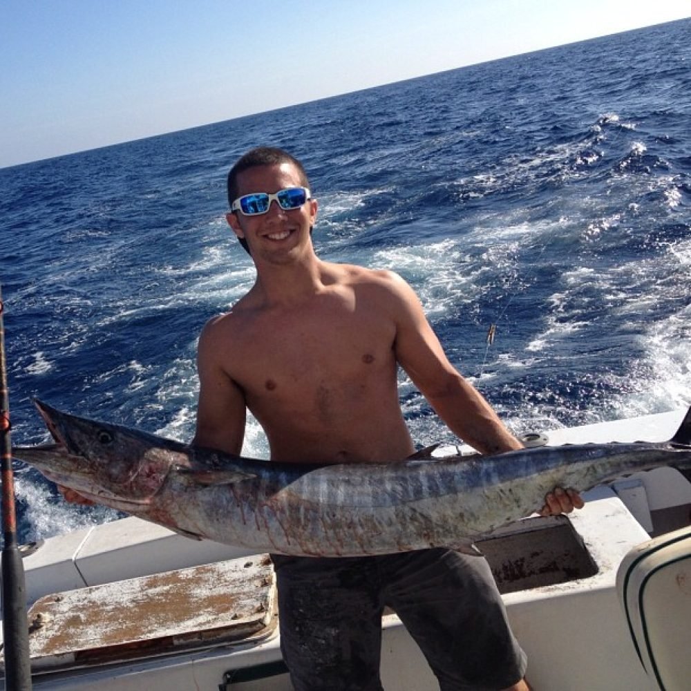 Wahoo Fishing Charters in Key West Smiling angler proudly holding a large wahoo on a boat during a Wahoo Fishing Charter in Key West with Fish Daily Charters, with the deep blue ocean in the background.